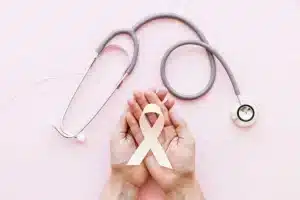 white awareness ribbon two hands with stethoscope pink background e1663582374733
