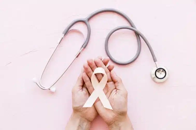 white awareness ribbon two hands with stethoscope pink background e1663582374733